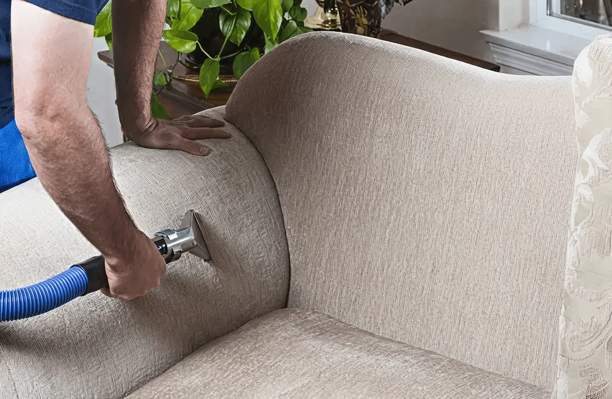 Professional upholstery cleaner deep-cleaning a fabric sofa with a handheld extraction tool and hose, Evansville, IN.